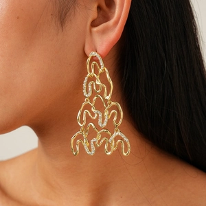 Close-up of gold oversized irregular wavy earrings with crystals on a female model