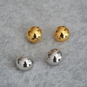 Close-up of polished gold and silver spherical stud earrings on soft fabric