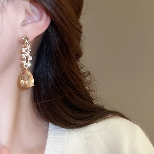 Close-up of a gold teardrop earring with amber gemstone worn by a model in soft light