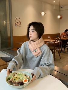 Detail view of pink knitted scarf with KN.STUDIO label worn in a cozy cafe setting