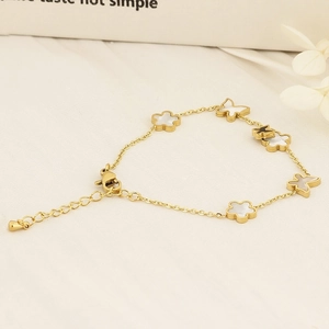 Adjustable gold butterfly and four-leaf clover charm bracelet on light fabric