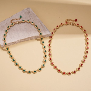 Vintage gold necklaces with green and red oval gemstones on a neutral stone display