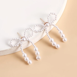 Close-up of handmade pearl bow earrings with elegant golden hanging fringe details