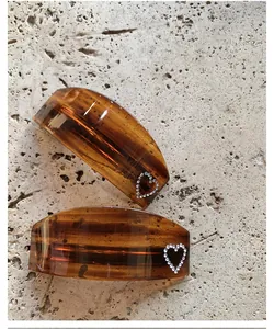 Detail of amber tortoiseshell hair clips with rhinestone heart accents on stone background