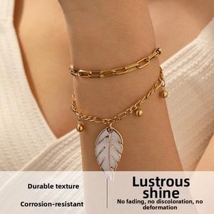 Close-up of dual-layer gold stainless steel bracelet with white enamel leaf charm and beads