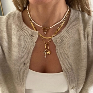 Detail of layered gold necklaces with heart pendant and pearl charm on neck