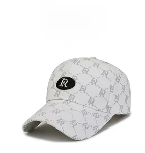 Detail of white baseball cap showing grey monogram pattern and black metal emblem plate
