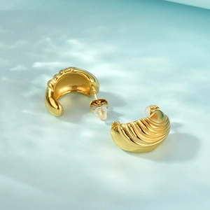 Macro detail of gold-plated irregular spiral earrings with shell-like textured metal finish