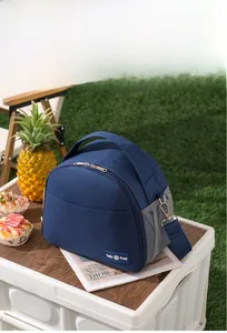 Outdoor leisure scene showing a blue insulated lunch bag with shoulder strap on grass