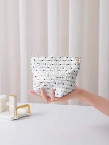 Borsa cosmetica in tessuto a pois e strisce con cerniera a fiore tenuta in mano
