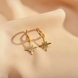 Macro detail of golden star hoop earrings with micro-inlaid zircon on silk fabric