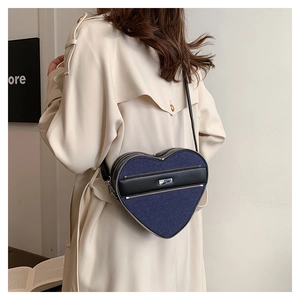 Detail view of heart-shaped crossbody bag in blue denim and black leather worn by model