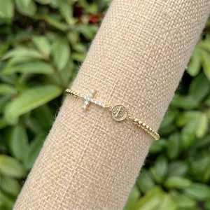 Dettaglio di un bracciale placcato oro 18k con croce di diamanti e medaglia religiosa