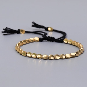 Detalle de la pulsera de cordón negro tejida con cuentas doradas y borlas decorativas