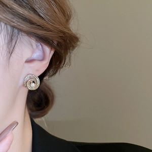 Nahaufnahme eines goldenen Spiralohrrings mit kleinen Kristallen und einer weißen Perle