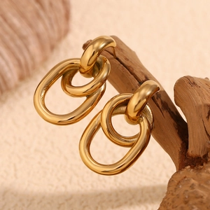 Détail de boucles d'oreilles créoles en acier doré 18 carats suspendues sur bois