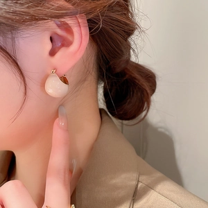 Close-up of a model wearing cream enamel C-shaped chunky hoop earrings with a gold finish