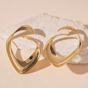 Close-up of golden irregular liquid metal earrings on a natural textured stone base
