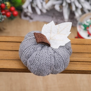 Grey knitted pumpkin decoration with white felt leaf on dark wooden surface for autumn