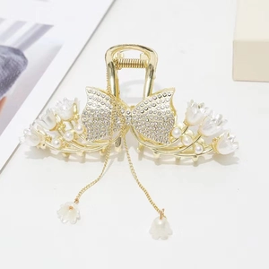 Detail of rhinestone bow hair claw with gold flower tassels and pearl accents