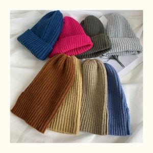 Flat lay of multiple colorful knitted beanies on soft white fabric showing soft texture