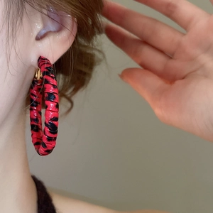 Gros plan d'une boucle d'oreille créole imprimé léopard rouge et noir sur modèle