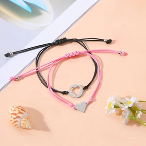 Detalle de pulseras trenzadas de corazón rosa y negro con accesorios de conchas y flores