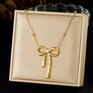 Détail d'un collier avec pendentif nœud doré, perle blanche et texture en métal martelé