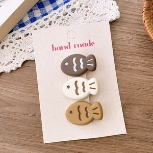 Three cute fish-shaped matte hair clips in brown and cream on a handmade card