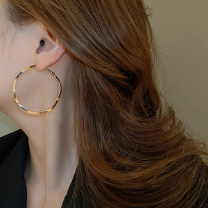Close-up of a large gold hoop earring on a model, showcasing minimalist metallic texture