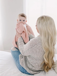 Soft pink cotton muslin baby swaddle blanket held by mother in cozy home setting