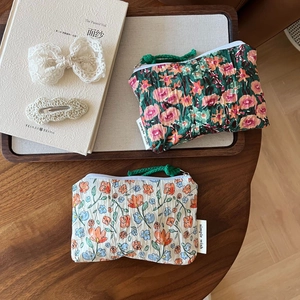 Détail de pochettes en coton à fleurs avec zip, poignée tissée et étiquette de marque