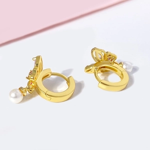 Détail de boucles d'oreilles papillon dorées avec zircons roses et perles élégantes