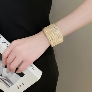 Close-up of wide golden cuff bracelet with brushed metal texture worn by a model