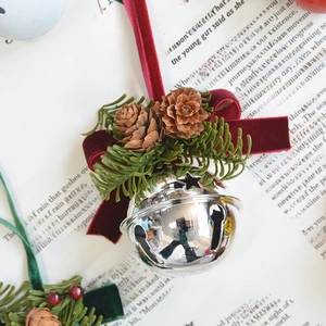 Silver bell Christmas ornament with a red velvet bow, pine cones and green needles