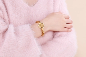 Close-up of gold Hamsa Hand bracelet with white pavé crystals on a soft peach background