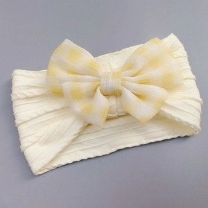 Detail of baby headband featuring cream knit fabric and a yellow plaid bow detail