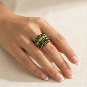 Detail of chunky gold ring with green crystals on a model hand with fabric background
