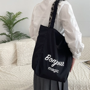 Detail of black canvas tote bag with leopard print strap and Bonjour magic text