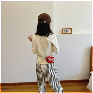 Detail of red heart-shaped butterfly bag worn with striped pants and brown baseball cap