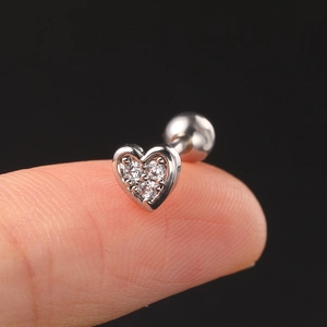 Macro view of heart-shaped zircon ear stud on fingertip showing small size and silver shine