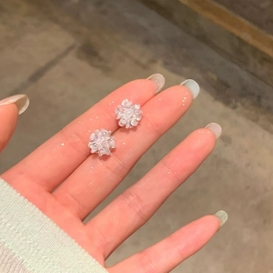 Macro view of crystal flower stud earrings held by fingers showing dainty size and detail