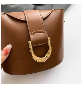 Detail view of brown leather bucket bag featuring a striking gold U-shaped metal buckle