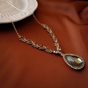 Macro shot of rose gold necklace featuring large gray teardrop pendant and crystal chain