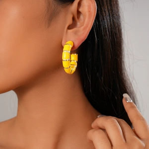 Close-up of a model wearing yellow and silver geometric C-shaped hoop earrings