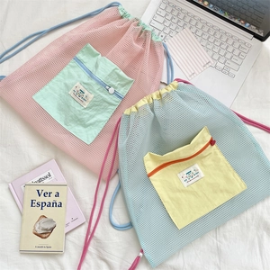 Detail view of mesh drawstring backpack with contrast zippers on a cozy bed background