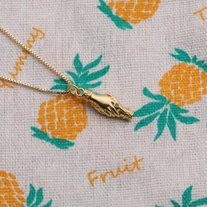 Detail of gold hand-shaped pendant with green gemstone and box chain on textured fabric