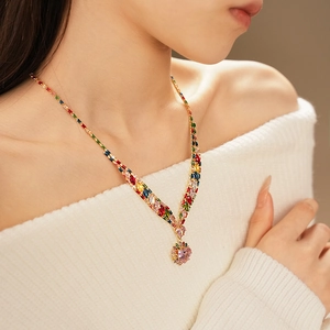 Detail of V-shaped gold necklace with colorful zircon gemstones and pink heart pendant