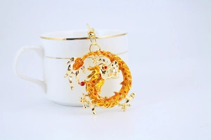 Detail of a golden dragon keychain pendant with red texture leaning on a tea cup