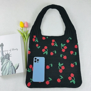 Detailed shot of black knit tote bag featuring red cherry patterns on textured fabric